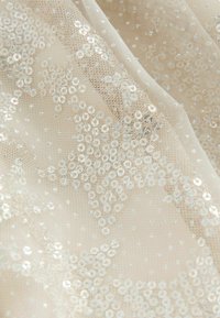 Tissu en maille beige avec des sequins blancs disposés en motifs d'étoiles, créant une surface texturée scintillante et décorative.