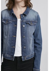 Giacca di jeans con una sfumatura da chiara a scura, chiusura con bottoni, due tasche sul petto e un design corto. Maniche lunghe e colletto classico.
