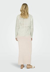 Cămașă lungă cu mâneci, perforată, de culoare verde deschis, cu modele decorative, asortată cu o fustă maxi ajustată, cu dungi, de culoare piersică și sandale plate.