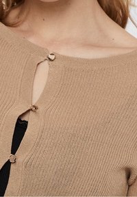 Cardigan a coste tan con design una spalla, dotato di un piccolo dettaglio a chiave e bottoni circolari color oro.