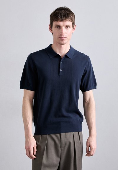 Marineblauwe gebreide poloshirt met een kraag, korte mouwen, gestructureerde panelen en drie knopen aan de voorkant. Gecombineerd met een op maat gemaakte broek.