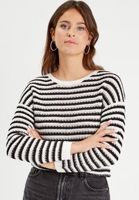 Black and white striped sweater with a round neckline, ribbed cuffs, and a loose knit texture. The stripes alternate in thickness.