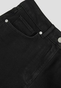 Los jeans de mezclilla negra presentan un primer plano de la cinturilla con un lazo para el cinturón, un botón de metal y un pequeño bolsillo delantero. La textura parece suave.