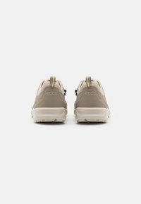 Sneaker beige con tomaia testurizzata, linguetta a contrasto e sistema di lacci neri. Presenta il marchio sul tallone e una suola imbottita.