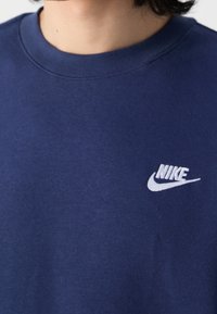 Námořnická modrá mikina s kulatým výstřihem, vyrobená z jemné tkaniny, s bílou vyšívanou logem Nike na hrudi. Jednoduchý a klasický design.
