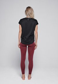 Zwarte sporttop met korte mouwen, gecombineerd met aansluitende bordeauxrode leggings met rode accentnaden, een gladde textuur en een subtiel logo bij de halslijn.