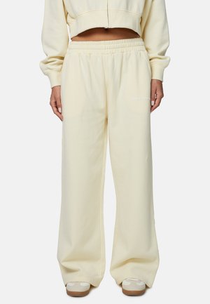 Pantalon de survêtement jaune clair avec une ceinture élastique, des jambes larges, et un logo imprimé en blanc sur la cuisse gauche. Fabriqué en tissu de coton doux.