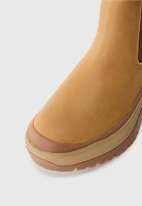 Tan leather boot with a smooth finish, rounded toe, and contrasting rubber sole. Features a low profile and subtle stitching detail near the ankle.