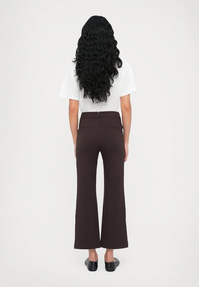 Braune Schlaghosen mit hoher Taille und aufgesetzten Taschen, kombiniert mit einem weißen T-Shirt. Glattes Material, mit einem verdeckten Reißverschluss hinten.