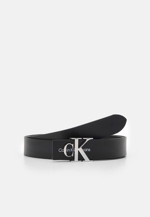 Černý kožený pásek s kovovou sponou stříbrné barvy s logem "CK" a natištěným textem "Calvin Klein Jeans" na popruhu. Hladký povrch.