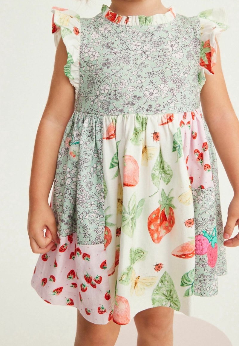 Tout-petit portant une robe patchwork avec des imprimés floraux, fraises et fruits, dotée de manches à volants et d'une taille froncée.