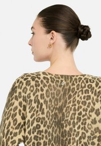 Suéter de punto con estampado de leopardo en tonos beige y marrón, con un escote ancho y un pequeño logo en la parte posterior. Textura suave.