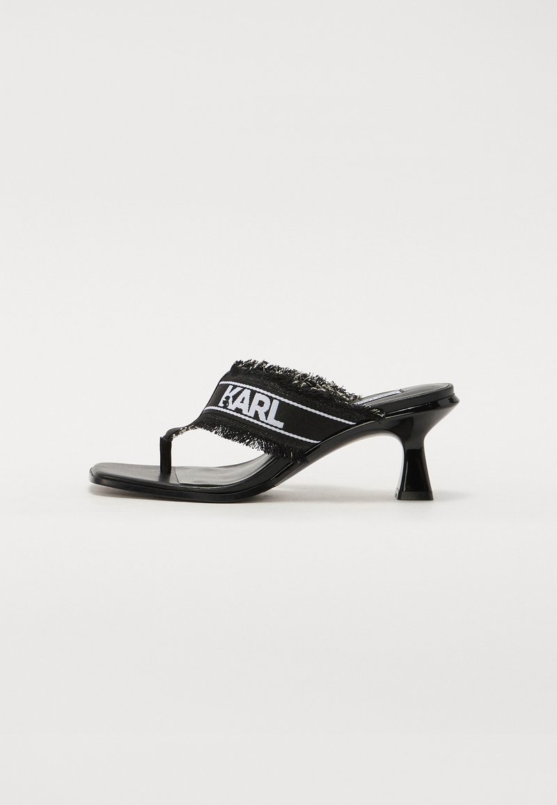 Black heeled sandals featuring a toe post design, fabric strap with fringe edges, and a white logo detail. Glossy patent finish.