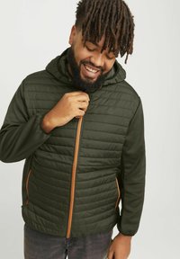 Veste matelassée vert foncé avec capuche, dotée d'une fermeture éclair orange et d'accents latéraux, fabriquée dans un tissu lisse et isolé.