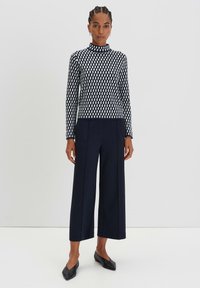 Maglione a righe navy con collo alto, abbinato a pantaloni larghi navy e ballerine nere. Presenta motivi geometrici in colori a contrasto.