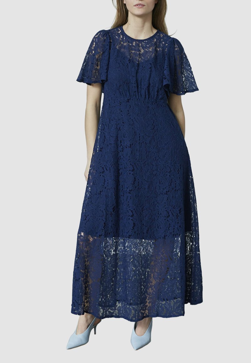 Mørkeblå blonde maxi kjole med korte, voluminøse ærmer og en gennemsigtig nederste sektion. Har blomstermønstre og en rund halsudskæring.