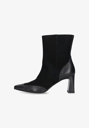 Zwarte enkelboot van een combinatie van suede en leer, met een spitse neus, een hak van 10 cm, brogue-details langs de rand en een gladde afwerking.