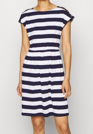 Femme portant une robe longueur genou avec des rayures horizontales bleu marine et blanc et des manches courtes avec bordure en dentelle.