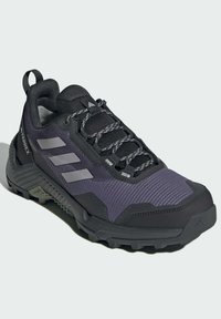Vandring sko med en svart och mörk lila tygöverdel, texturerad mesh, grå detaljer och en robust sula för bra grepp. Snörning med ett dra-rep.