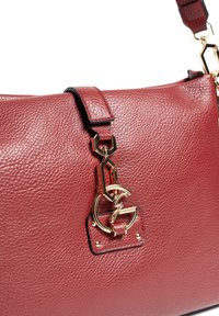 Bolso de mano de cuero rojo con una superficie texturizada, herrajes dorados, una correa con eslabones hexagonales y un destacado detalle de logo en la parte frontal.