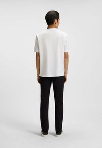 Maglietta bianca a maniche corte con colletto tondo, abbinata a pantaloni neri slim-fit e sneakers casual, vista da dietro.