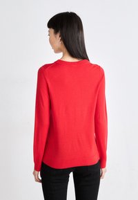 Κόκκινο μακρύ μανίκι πουλόβερ από λείο πλεκτό ύφασμα, με στρογγυλή λαιμόκοψη και ριγωτό τελείωμα. Η πλάτη έχει εφαρμοστή σχεδίαση χωρίς επιπλέον σχέδια.