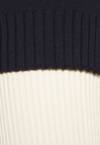 Strickpullover mit einem dunkelblauen strukturierten Rippenbund oben und einem kontrastierenden cremefarbene Rippenkörper.