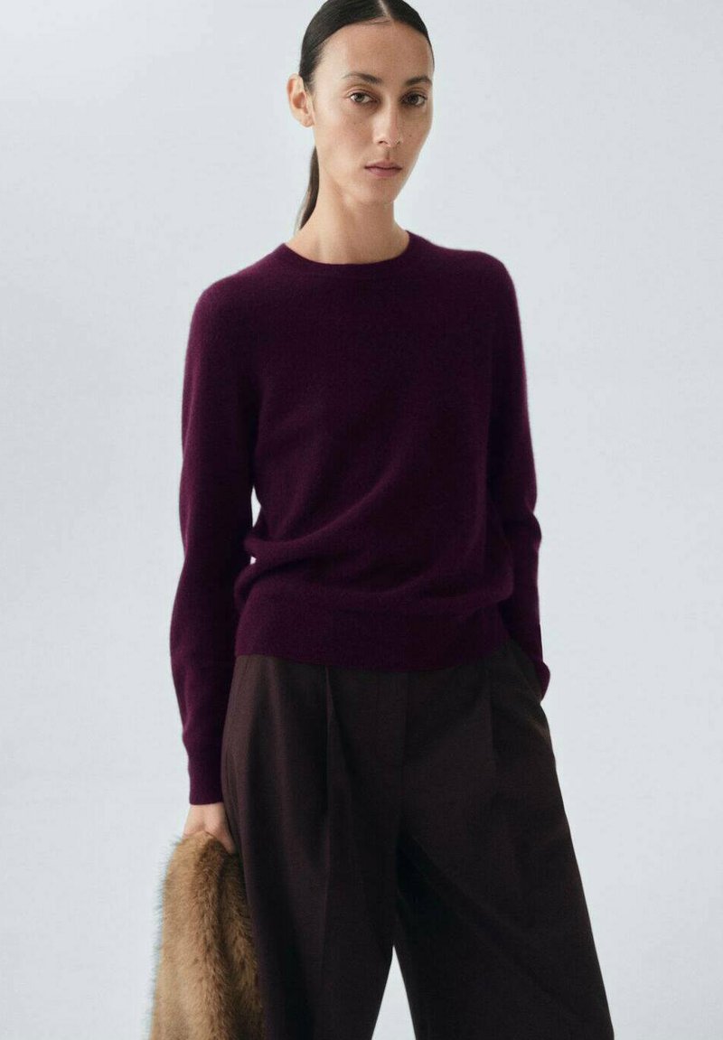 Burgunderfarbener Strickpullover mit Rundhalsausschnitt, getragen mit dunkelbraunen weit geschnittenen Hosen. Die Textur wirkt weich, mit eng anliegenden Ärmeln und einer lockeren Passform.