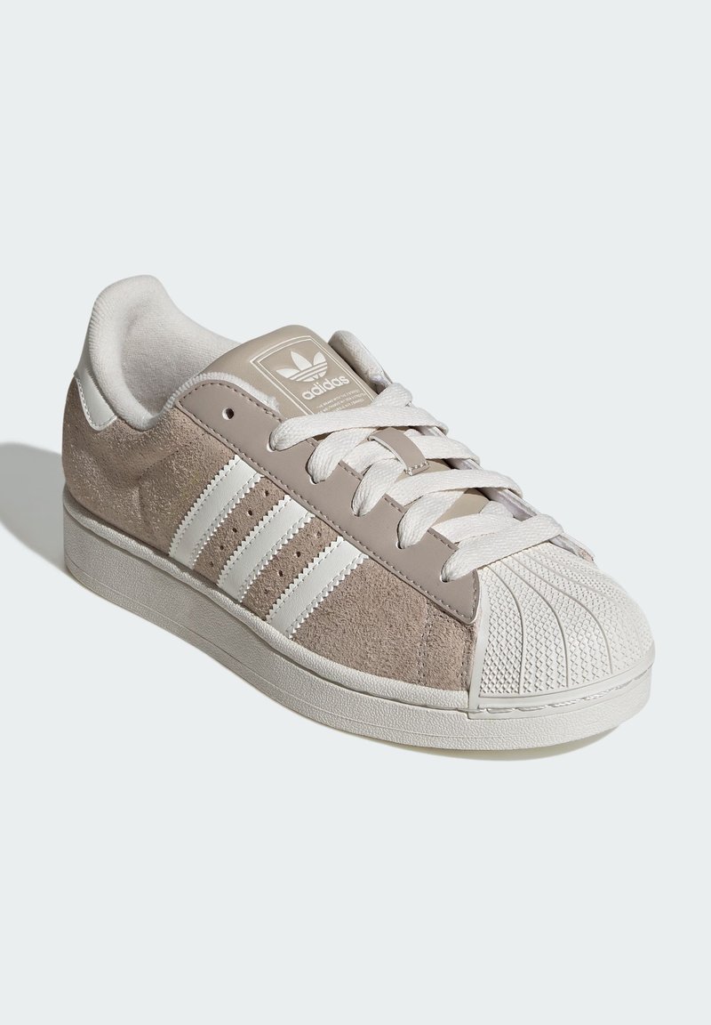 Baskets beiges avec accents blancs. Tige en daim et cuir, trois bandes blanches sur le côté, embout en caoutchouc texturé et lacets.