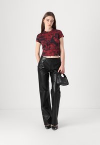 Red graphic cropped t-shirt with bold black design paired with high-waisted black leather pants. Model holds a small black handbag.