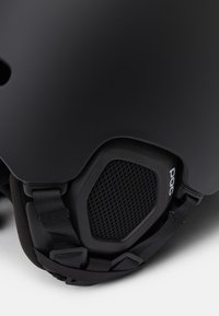 Schwarzer Skihelm mit einer glatten Außenschale, gepolstertem Innenbereich, verstellbaren Riemen und Belüftungsnetz an der Seite für Luftzirkulation.