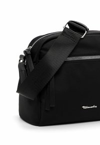 Borsa a tracolla nera realizzata in tessuto, dotata di una chiusura zip, tracolla regolabile e una piccola tasca frontale con dettagli in nappe. Logo sul lato.