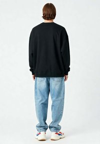 Felpa nera oversize con polsini e orlo a coste, abbinata a jeans baggy azzurri e sneakers bianche con dettagli rossi e blu.