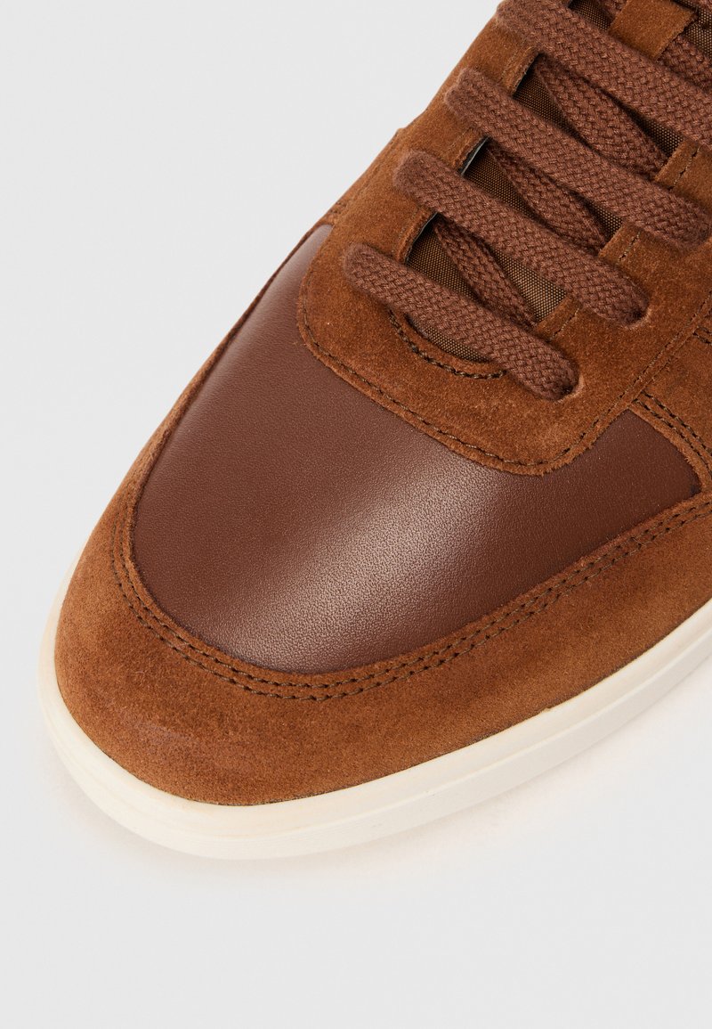 Baskets marron avec une combinaison de cuir lisse et de suède, avec un bout arrondi, des lacets texturés et une semelle blanche.
