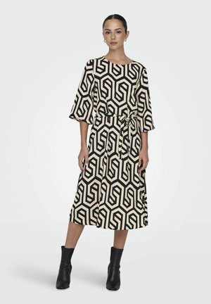Zwarte en beige geometrisch patroon jurk met driekwart mouwen, een ronde halslijn en een strik taille, gecombineerd met zwarte enkellaarsjes.