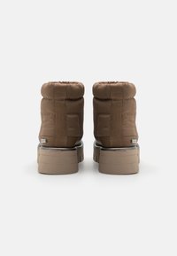 Bottes marron à la cheville avec tissu matelassé, empeigne rembourrée et semelle plateforme épaisse. Comprend un accent logo près du talon.