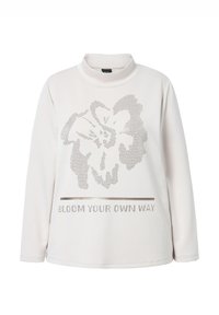 Top a maniche lunghe e collo alto in crema con un design floreale e la scritta "BLOOM YOUR OWN WAY" in borchie argentate sul davanti. Tessuto morbido.