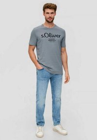 Gray short-sleeve t-shirt with black printed text, paired with light blue jeans and white sneakers. Casual, fitted design.