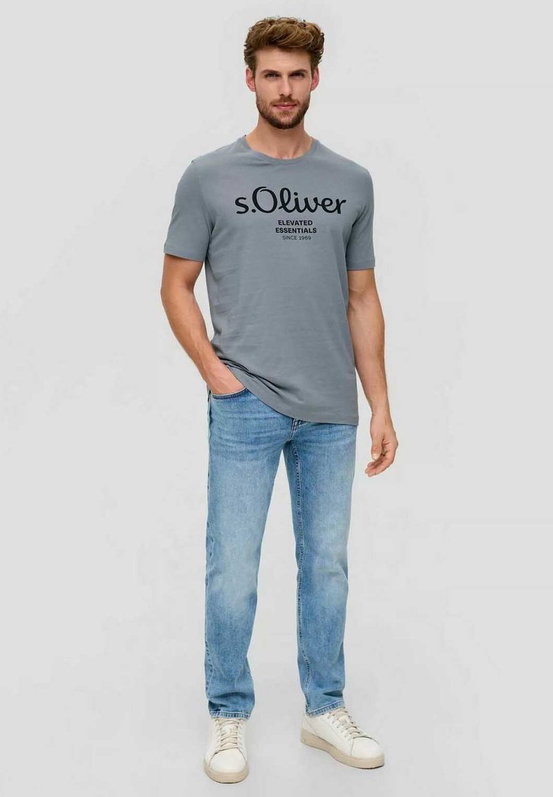 Gray short-sleeve t-shirt with black printed text, paired with light blue jeans and white sneakers. Casual, fitted design.