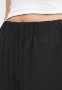 Pantalon noir taille haute avec une ceinture élastique, présentant une texture douce et une finition de tissu lisse, avec des détails subtils de plis.