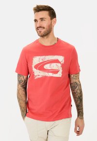 Rød bomulds T-shirt med et hvidt grafisk logo på fronten, korte ærmer og rund hals. Har en afslappet pasform og et logo-tag på siden.