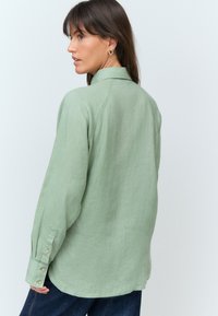 Light green long-sleeve shirt with a soft texture, buttoned cuffs, and a relaxed fit. Features a classic collar and curved hem.