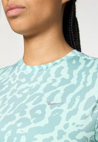 Cămașă sport Nike de culoare verde mentă deschis, cu un model ondulat. Textură netedă, guler în formă de cerc și un mic logo argintiu pe piept.