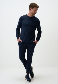 Marineblauer Rundhals-Sweatshirt kombiniert mit passenden schmal geschnittenen Jogginghosen. Weicher Stoff, minimalistisches Design, mit Seitentaschen und sportlichen Sneakers.