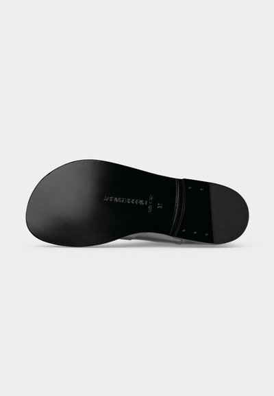 Semelle d'une chaussure habillée noire montrant une semelle en cuir lisse avec le nom de la marque en relief et une zone de talon cousue avec des rivets métalliques.
