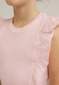 Ljusrosa linne med ribbat mönster, med volangdetaljer på axlarna. Slät halsringning och figurnära silhuett.