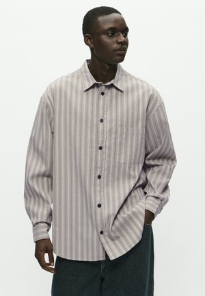 Relaxed-fit button-up shirt in light purple and cream stripes, featuring a chest pocket and dark buttons, made from a soft, textured fabric.