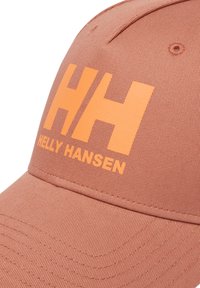 Gorra de tela coral con una forma estructurada. Presenta un audaz "HH" naranja y el texto "HELLY HANSEN", con costuras visibles y una superficie suave.