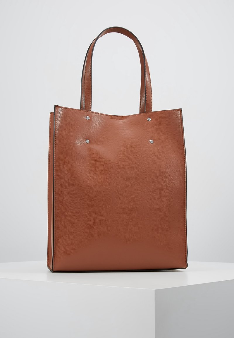 Brązowa torba typu tote ze skóry, z dwoma uchwytami, prostokątnym kształtem, teksturowanym wykończeniem i srebrnymi akcentami metalowymi z przodu jako detal.
