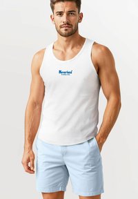 Weißes Tanktop mit blauem Drucktext, kombiniert mit hellblauen Shorts. Das Tanktop hat einen runden Halsausschnitt und eine lockere Passform.